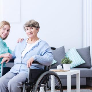 A caregiver assisting an elderly woman in a wheelchair in a cozy living room setting.
