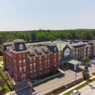 Aerial view of a historic red brick hotel with a parking lot surrounded by trees on a sunny day.
