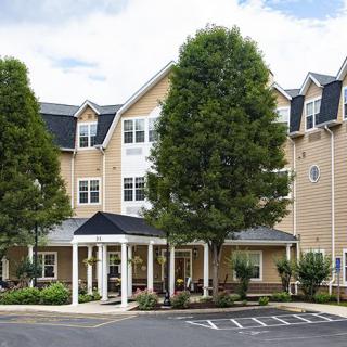 A residential building with a welcoming entrance surrounded by trees and a parking area.