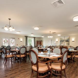 A spacious and elegantly furnished dining room with multiple tables and chairs, featuring warm lighting and a wooden floor.