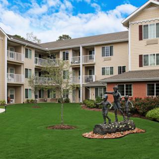 A well-maintained residential apartment building with a green lawn and sculpture in the courtyard.