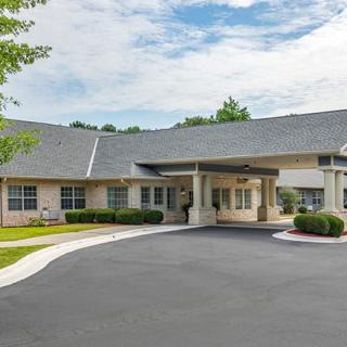 A building with a driveway and entrance surrounded by trees under a partly cloudy sky.