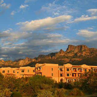 A warm sunset casts a golden hue over a desert landscape with mountains in the background and a building in the foreground.