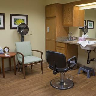 A well-equipped salon room with a hair dryer, chairs, sink, and mirror.