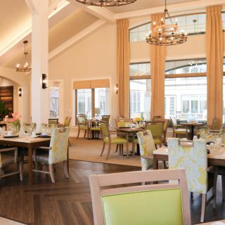 A spacious restaurant dining area with elegant chandeliers, large windows, and neatly arranged tables.