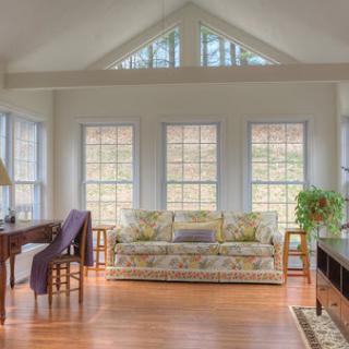 A bright and inviting living room featuring large windows, a comfortable sofa, and warm wooden flooring.