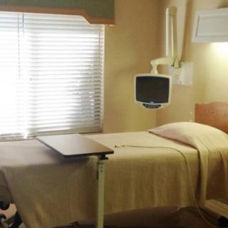 A tidy hospital room with a bed, side table, and wall-mounted television.