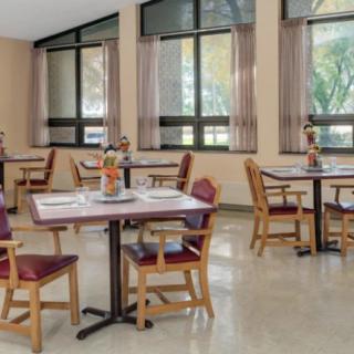 A cozy dining area with neatly arranged tables and chairs, illuminated by natural light from large windows.