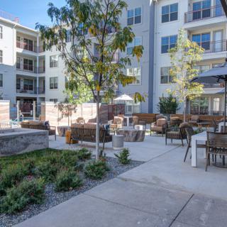 A modern apartment complex featuring an outdoor seating area with landscaping.