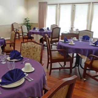A well-set dining area with tables covered in purple tablecloths, complete with place settings and seating.