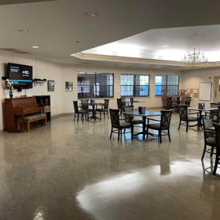 A spacious dining area with tables and chairs arranged for guests, featuring a television and ample natural light.