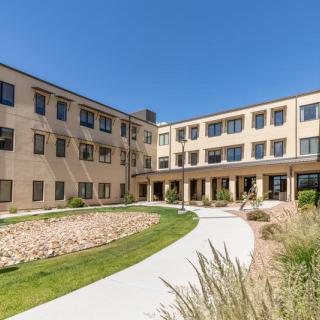 A sunny exterior view of a multi-story apartment building with landscaped surroundings and a curved pathway.