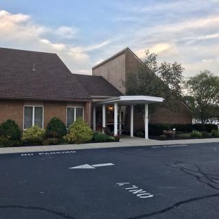 A one-story brick building with a covered entrance and an adjacent parking lot under a partly cloudy sky.