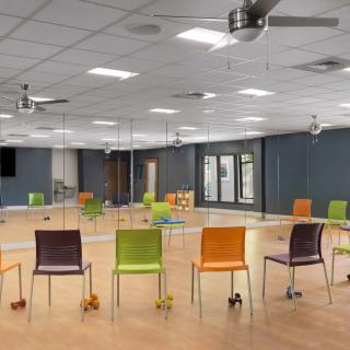 An empty exercise room with colorful chairs lined up in front of mirrors.