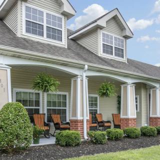 A charming residential house with a spacious front porch and greenery.
