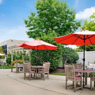 A sunny outdoor patio with tables and red umbrellas surrounded by lush greenery.
