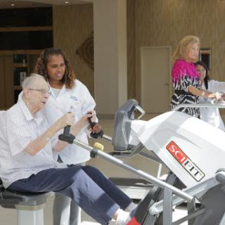 A caregiver assists a senior individual using exercise equipment for rehabilitation.