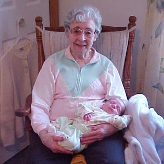 An elderly woman sitting in a rocking chair holding a baby indoors.