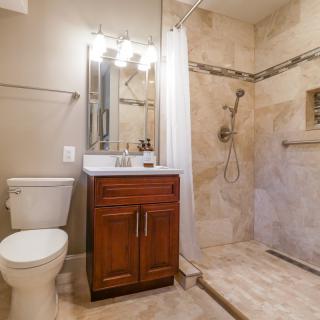 A modern bathroom with a wooden vanity, walk-in shower, and tile flooring.