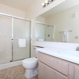 A clean and bright bathroom with a shower, toilet, sink, and mirror.