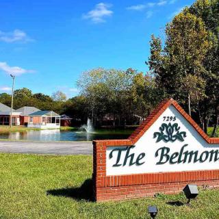 A scenic view of a brick sign for 'The Belmont' with a pond and fountain in the background.