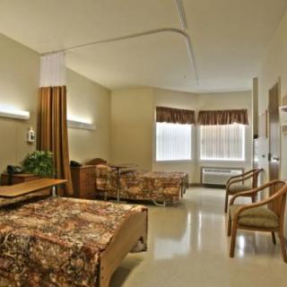 A clean and well-lit hospital room with a single bed, chairs, and curtains.