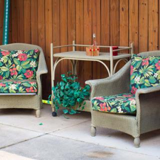 A cozy outdoor seating area featuring two floral-patterned chairs and a small table against a wooden backdrop.