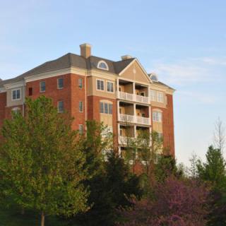 A multi-story brick apartment building surrounded by trees under a clear sky.