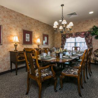 A traditional dining room with a large wooden table set for a meal, featuring ornate chairs and a central chandelier.