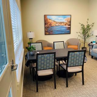 A cozy meeting room with a table and chairs, decorated with artwork, lamps, and an indoor plant.