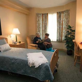 A cozy hospital room featuring a bed, chairs, and a warm ambiance with two people engaged in conversation.