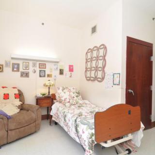 A cozy bedroom with a single bed adorned in floral bedding, an armchair, and various wall decorations.