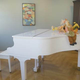 A stylish white grand piano elegantly placed in a cozy living room setting, adorned with a playful figure and colorful artwork.