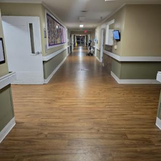 A view of a well-lit hospital hallway featuring wooden flooring and framed artwork on the walls.
