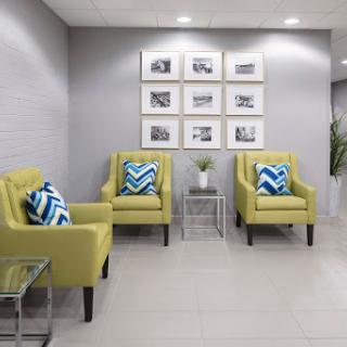 A modern waiting area featuring cozy yellow chairs with geometric patterned pillows, minimalistic dcor, and framed photographs on the wall.
