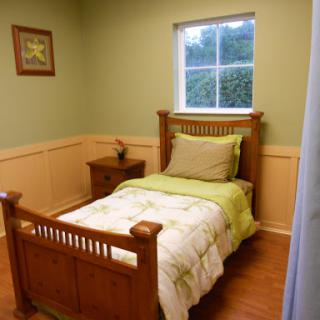 A cozy bedroom featuring a single wooden bed with green bedding and a serene ambiance.