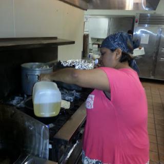 A chef pouring oil into a pot while preparing food in a restaurant kitchen.