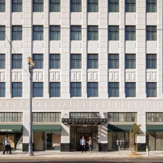 A view of an urban building facade with multiple windows, featuring people walking along the sidewalk.