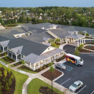 An aerial view of a building complex with surrounding greenery and a parking lot.