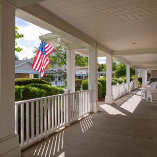 A sunny, peaceful porch featuring an American flag and white railing.