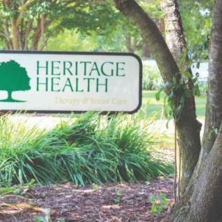 A sign for Heritage Health surrounded by trees and greenery.