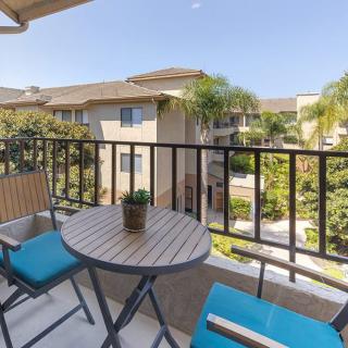 A balcony with a small table and chairs, overlooking an apartment complex on a sunny day.