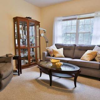 A cozy living room featuring a sofa, coffee table, and glass cabinet with a large window allowing natural light.