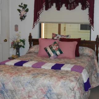 A cozy bedroom with a floral bedspread, decorative pillows, and a flower arrangement on the nightstand.