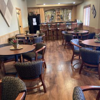 An empty dining area with tables and chairs, featuring a bar in the background.