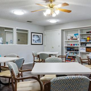 A well-lit room with tables, chairs, and shelves containing various items.