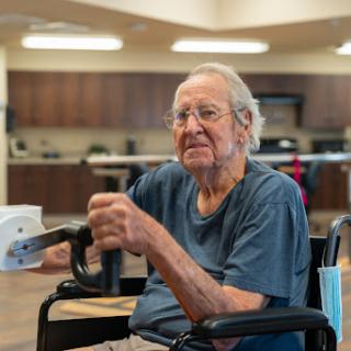 An elderly man sitting in a wheelchair, smiling and enjoying his time in a care facility.