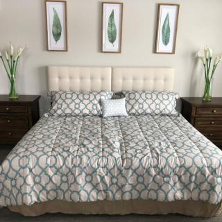A neatly arranged bedroom featuring a bed with patterned bedding, three framed artworks above the headboard, and vases with flowers on each nightstand.