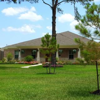 A single-story brick house with a well-maintained lawn and surrounding trees in a suburban setting.
