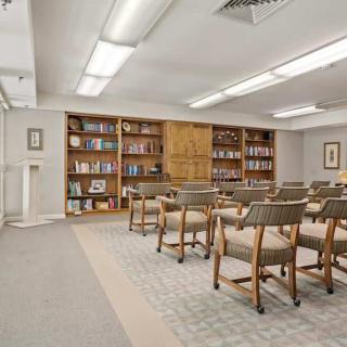 A quiet library setting with rows of chairs facing bookshelves filled with various books.